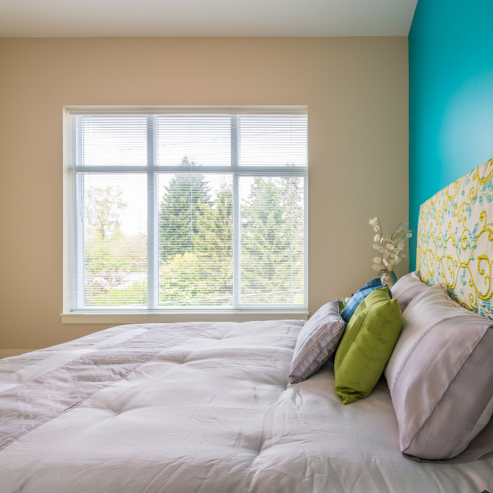 Bright bedroom with colorful accent pillows and a large window offering a serene view of trees and greenery.