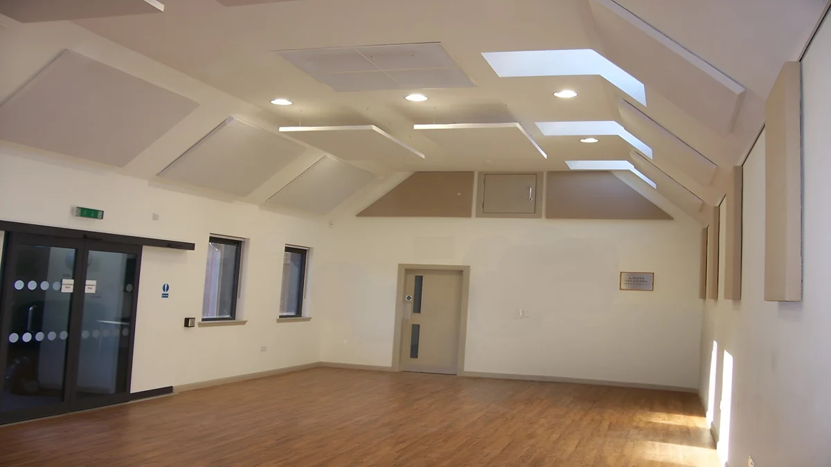 Cream acoustic panels on the pitched ceiling and walls of Bowsden Village Hall, with rooflights and a wooden floor.