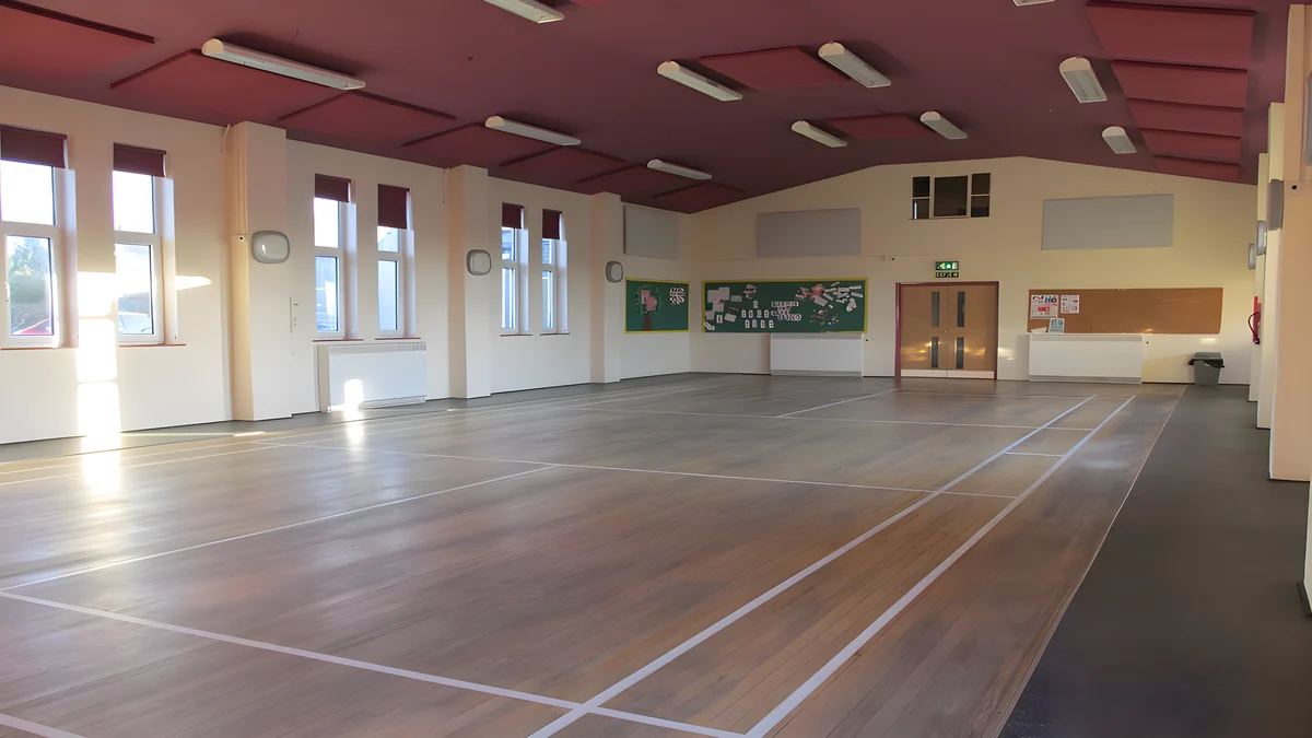 Grey acoustic panels on the dark red ceiling and upper walls of Burton-in-Kendal Memorial Hall, above a marked wooden sports floor.