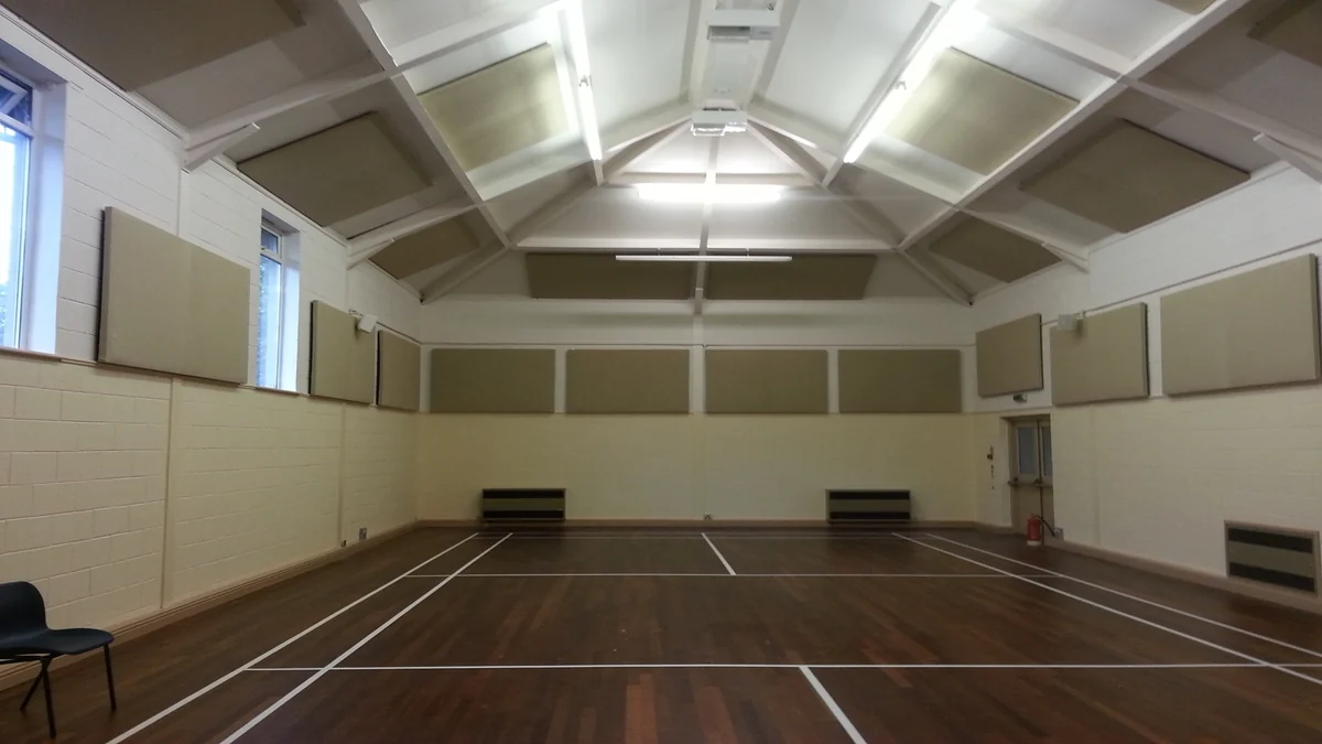 Acoustic panels between the white roof beams and on the upper walls at Natland Village Hall, above a wooden sports floor.