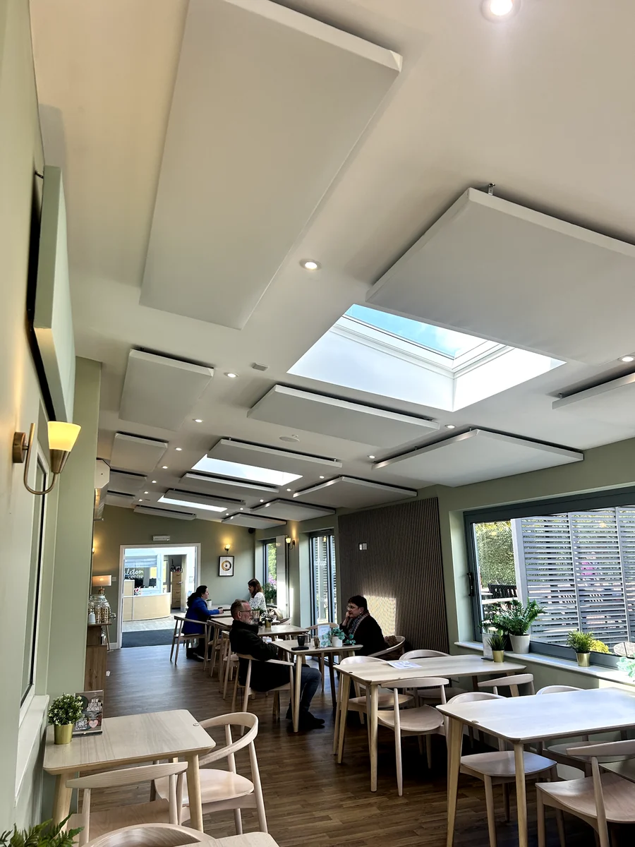White acoustic ceiling panels above tables beside large windows in Poppleton Community Centre café.