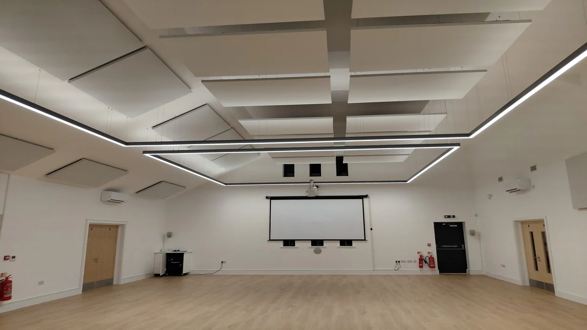 Rows of white suspended acoustic panels above a spacious hall with a projection screen at Warboys Community Centre.