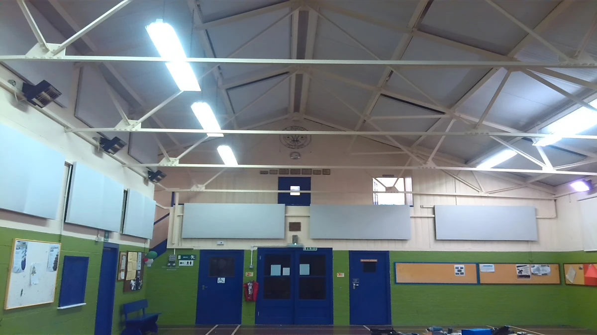 White acoustic wall panels above the green lower walls and blue doors of the 1st Ashtead Scout Hut, beneath exposed white roof trusses.