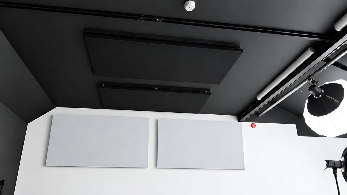 Dark acoustic panels beneath a black studio ceiling and a light grey wall panel beside a white backdrop at Giant Leap Productions.