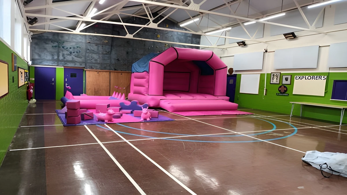 White acoustic wall panels around the 1st Ashtead Scout Hut, looking across its marked floor towards a pink inflatable activity area.