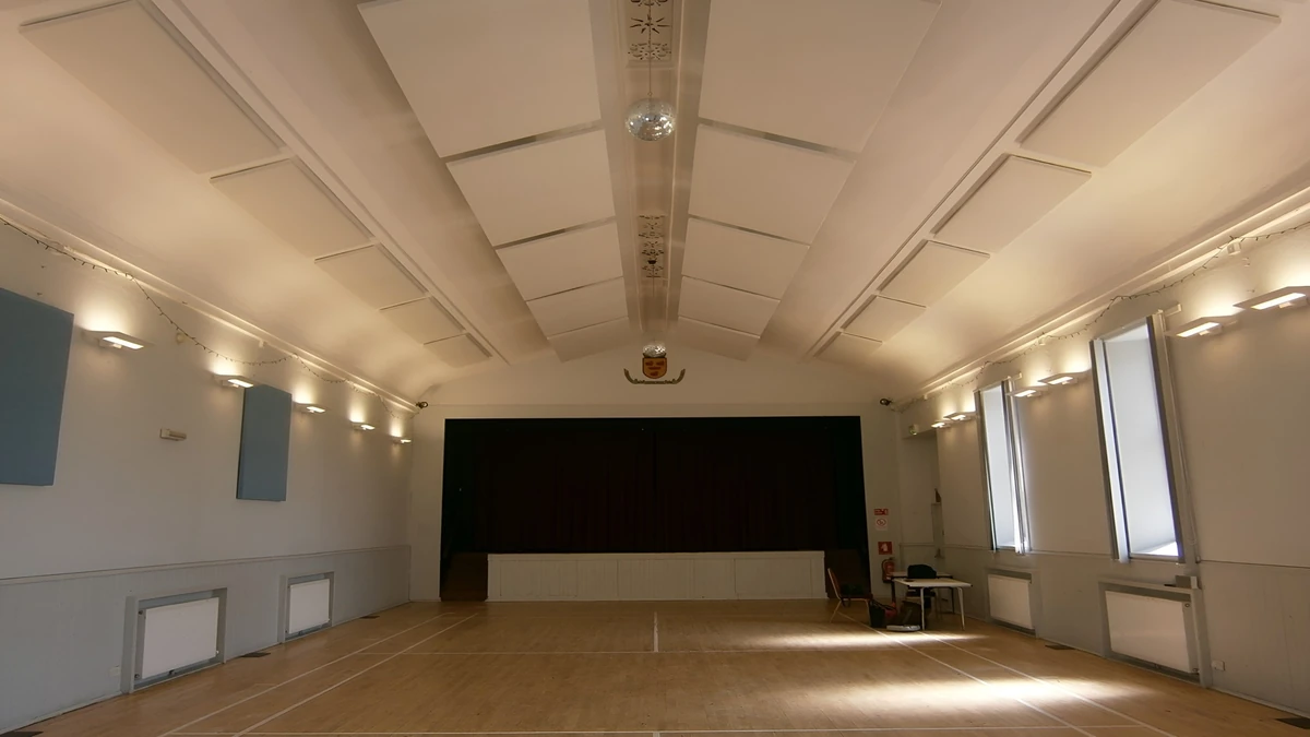 Rows of white ceiling panels and blue-grey wall panels in Cromarty Victoria Hall, looking across the wooden floor towards the stage.