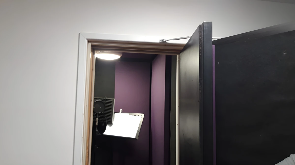 An open door reveals purple and dark acoustic treatment, a microphone and a music stand inside the Giant Leap Productions vocal booth.