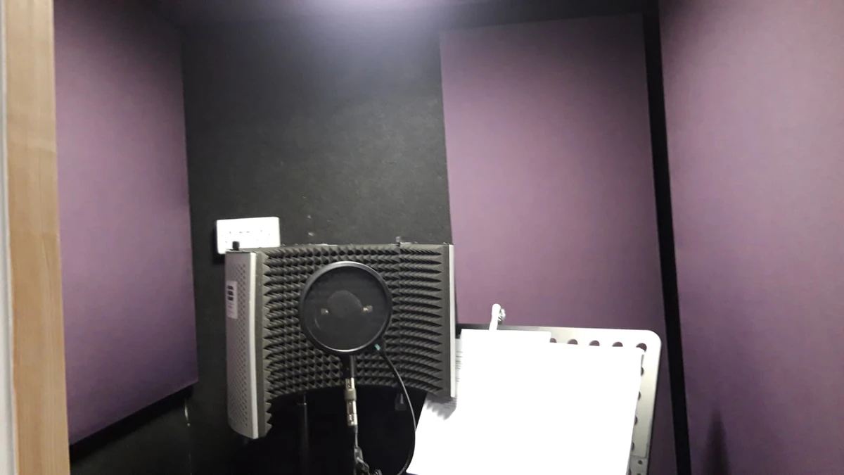 Purple and dark acoustic wall panels around a microphone with a curved reflection filter and a music stand inside the Giant Leap Productions vocal booth.