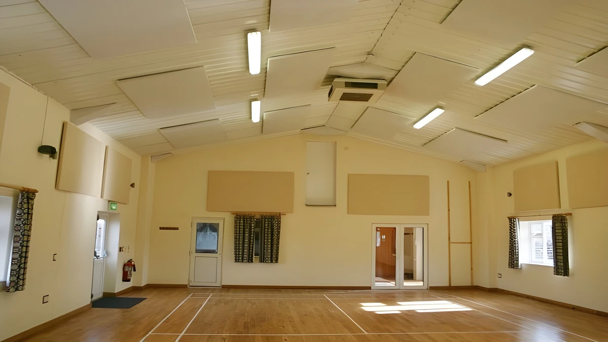 Cream acoustic wall panels and white ceiling panels in Halwell and Moreleigh Village Hall, above a marked wooden floor.