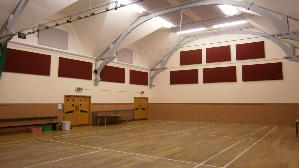 Red acoustic wall panels around a wooden sports floor beneath white roof beams at Tayside Institute Community Centre.