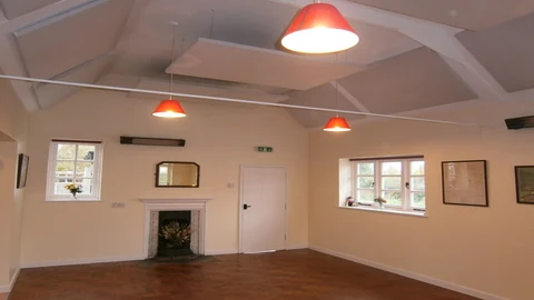White suspended ceiling panels between exposed beams and red pendant lights in Oxenton Village Hall.