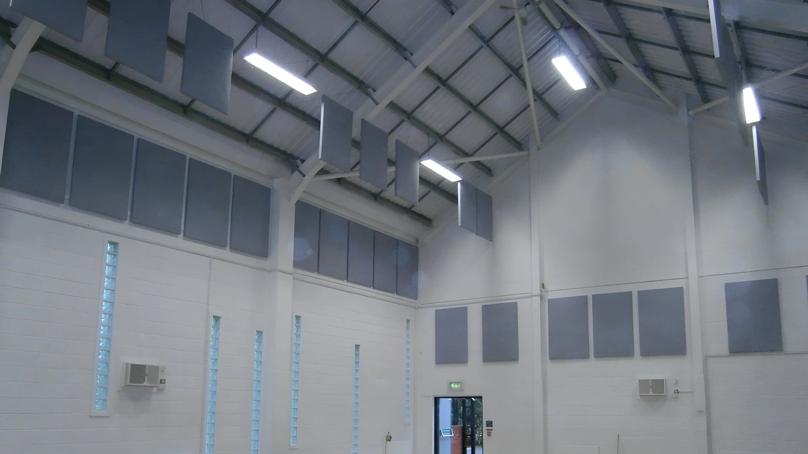 Grey acoustic wall panels and vertical suspended baffles beneath the high roof of Scartho Village Community Centre sports hall.
