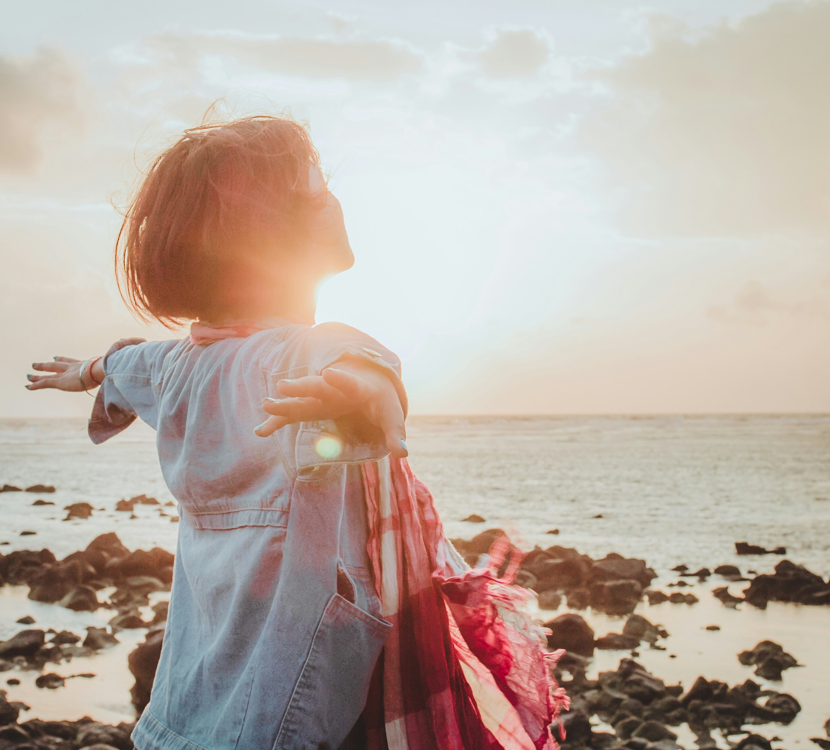 A woman facing the sunrise over the ocean coast with arms spread wide. A woman facing the sunrise over the ocean coast with arms spread wide.