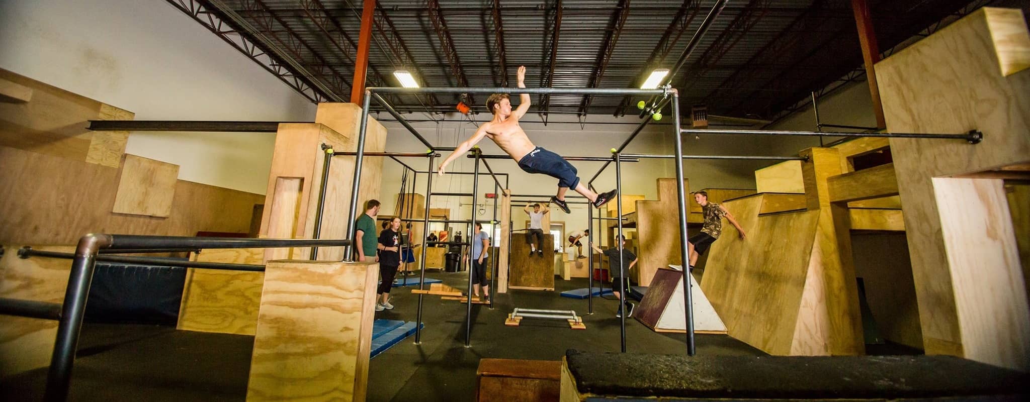 A perfectly-timed photo of an athlete in the middle of a flying release between a cage of bars. Several people in the background are looking on in stunned disbelief.