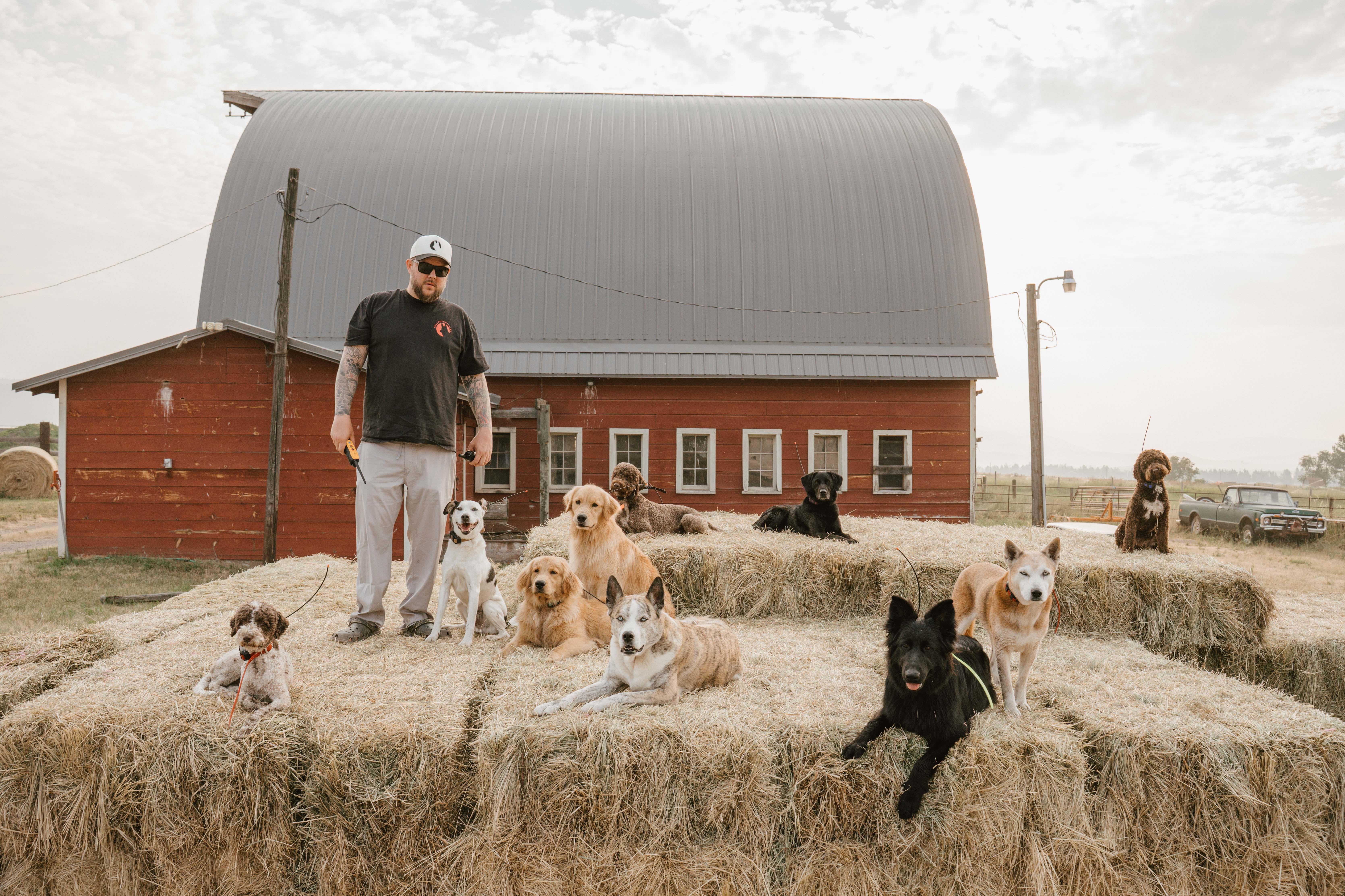 Dillon Mitchell stands in front of a red barn with nine dogs sitting on hay bales