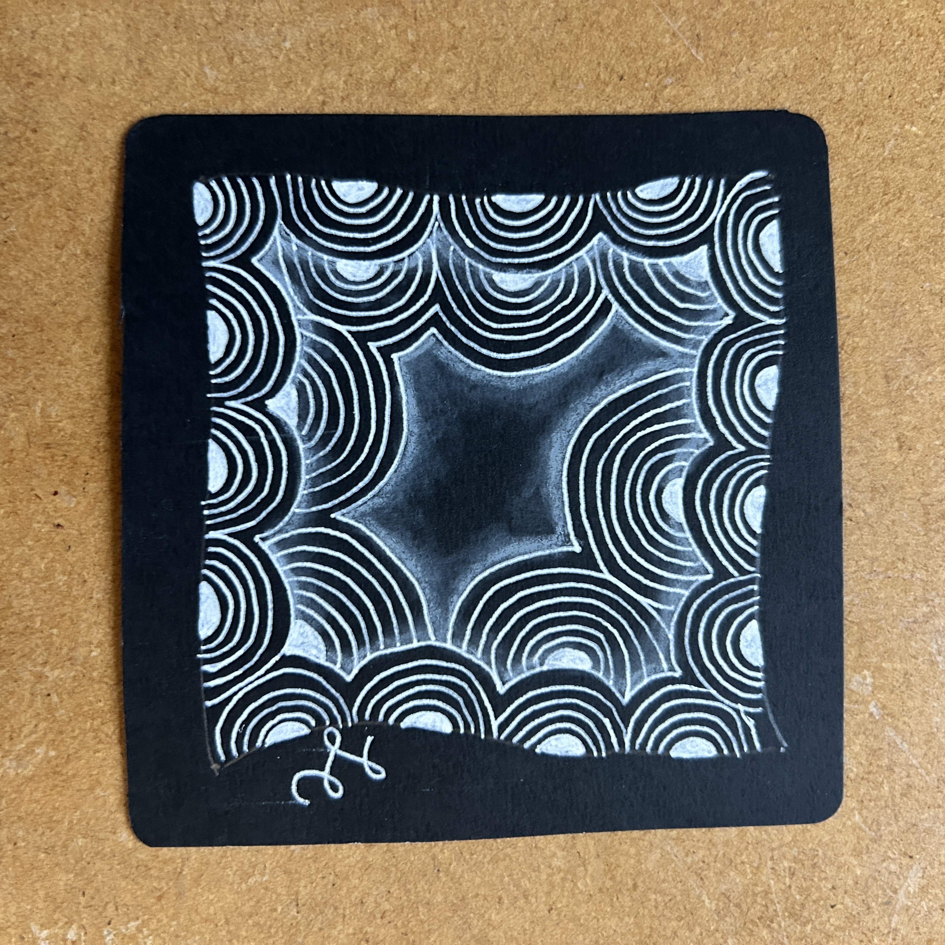 A black paper tile with the tangle Crescent Moon drawn on it in white. A black paper tile with the tangle Crescent Moon drawn on it in white.