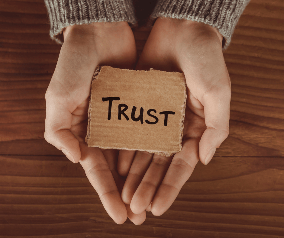 A close up on someone's hands. In their hands is a piece of card saying the word TRUST.