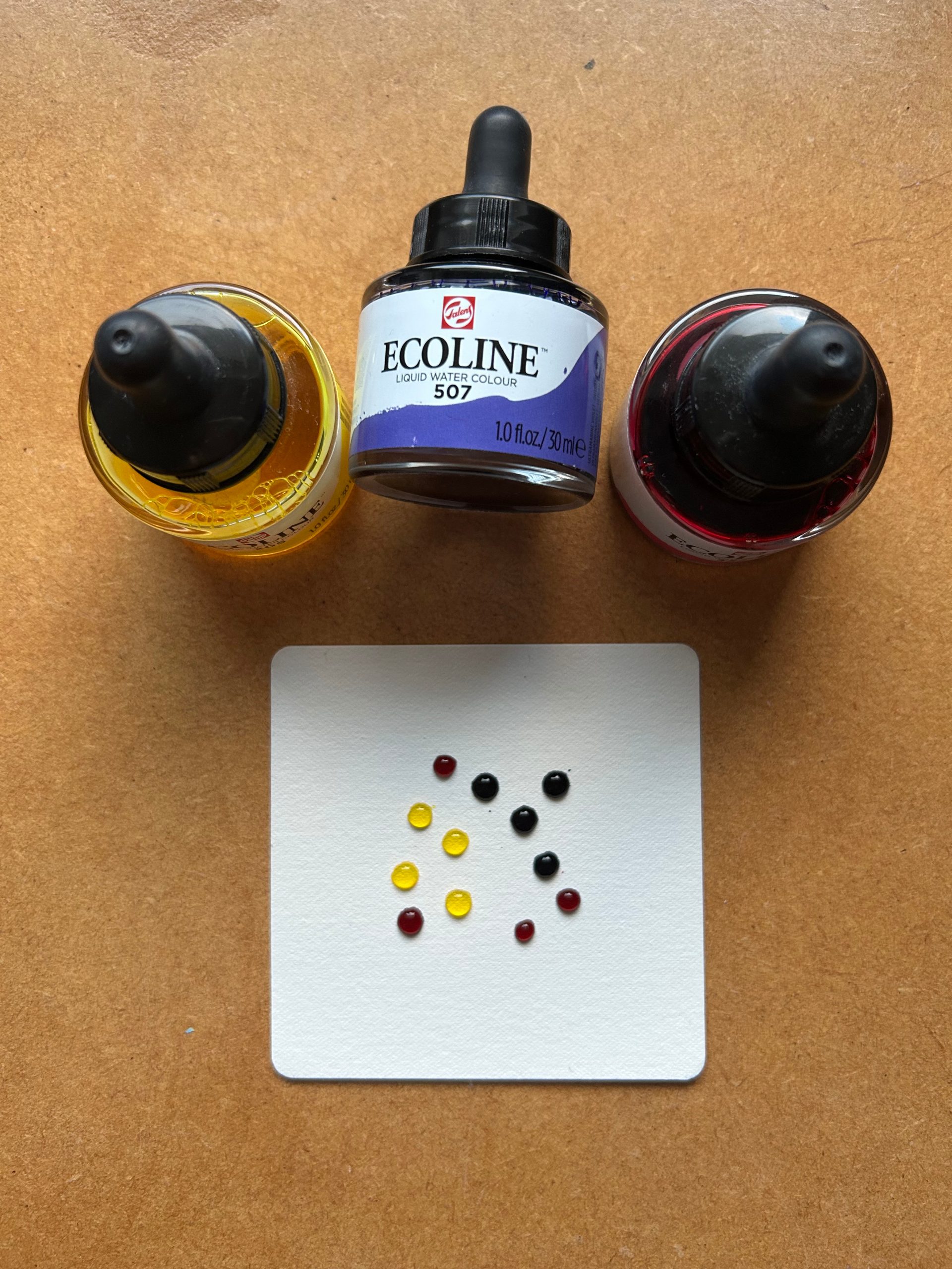 Lisa Crow CZT's prepped tile ready for a map tangling project. Droplets of liquid water colour can be seen sitting on the surface of a paper tile. There are three colours of ink bottle in the photo - yellow, purple and pink.