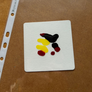 A plastic folder sits on top of a tile prepped with different colours of liquid watercolour. Tile has been prepped by Lisa Crow CZT.