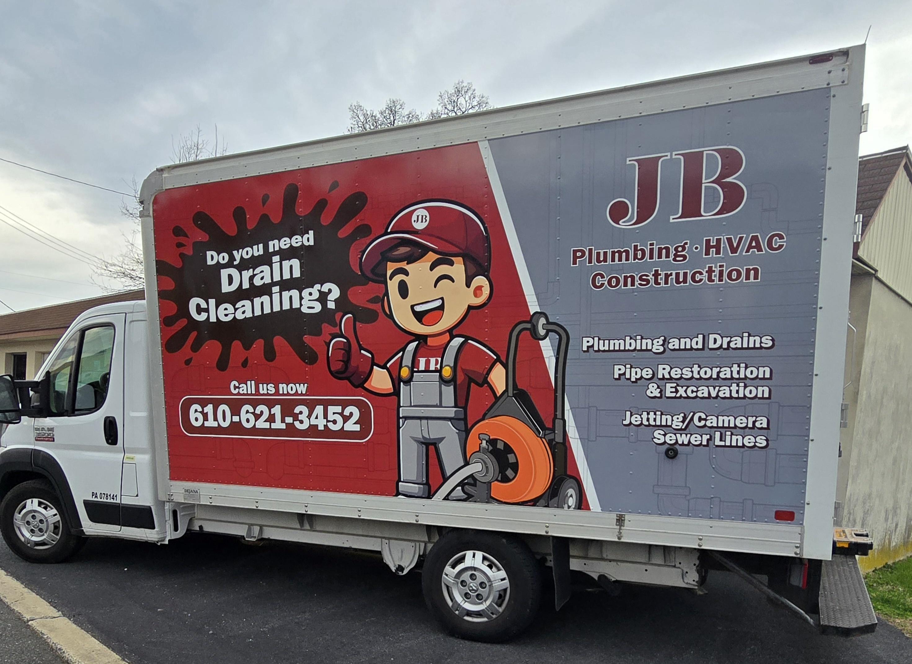 A professionally wrapped box truck for JB Plumbing HVAC & Construction featuring a cartoon plumber mascot, drain cleaning promotion, and a list of services including plumbing, HVAC, pipe restoration, and sewer line jetting/camera work. - JB Plumbing HVAC & Construction