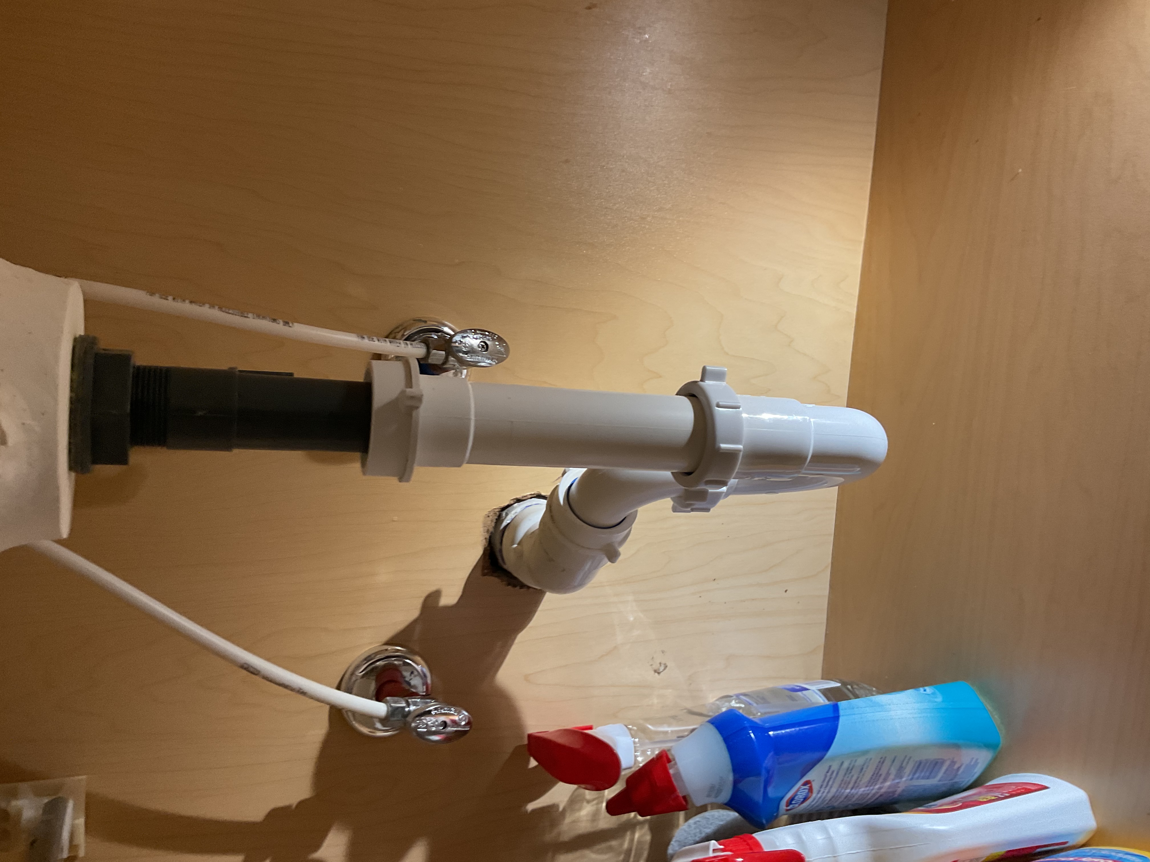 White PVC P-trap under a sink, joined to the drain tailpiece and supply shut-off valves