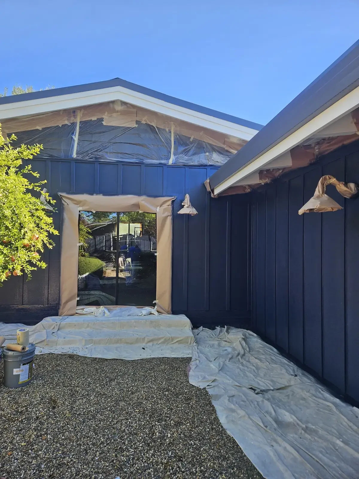 Navy board-and-batten exterior with windows and fixtures masked during painting