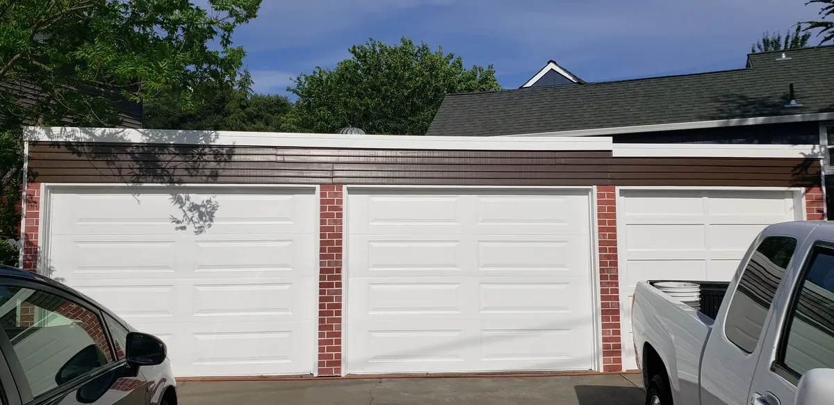 Three white garage doors with freshly painted brown trim and red brick columns