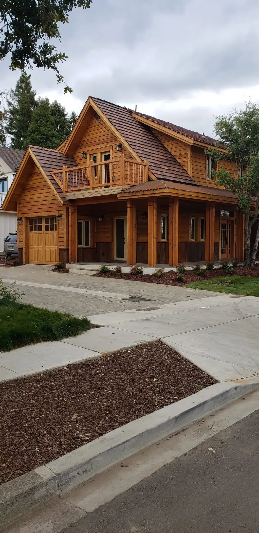 Two-story cedar home with freshly stained siding, balcony, and porch posts
