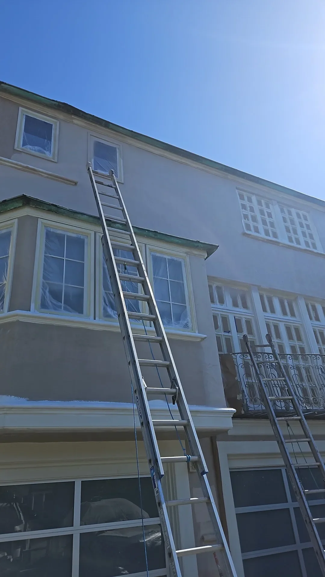 Stucco home with masked windows and ladders during exterior painting prep