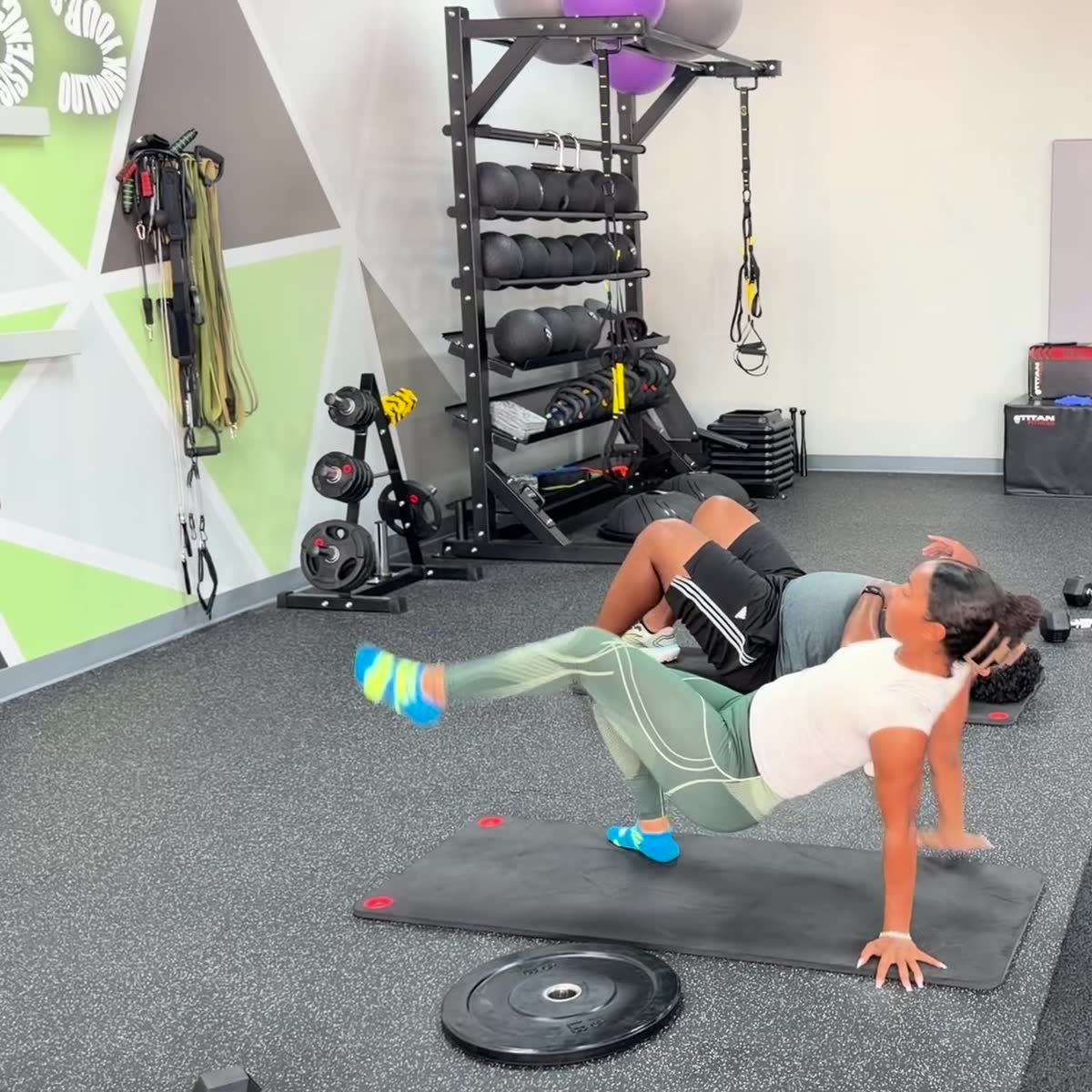 Two members holding side plank beside the medicine ball rack.
