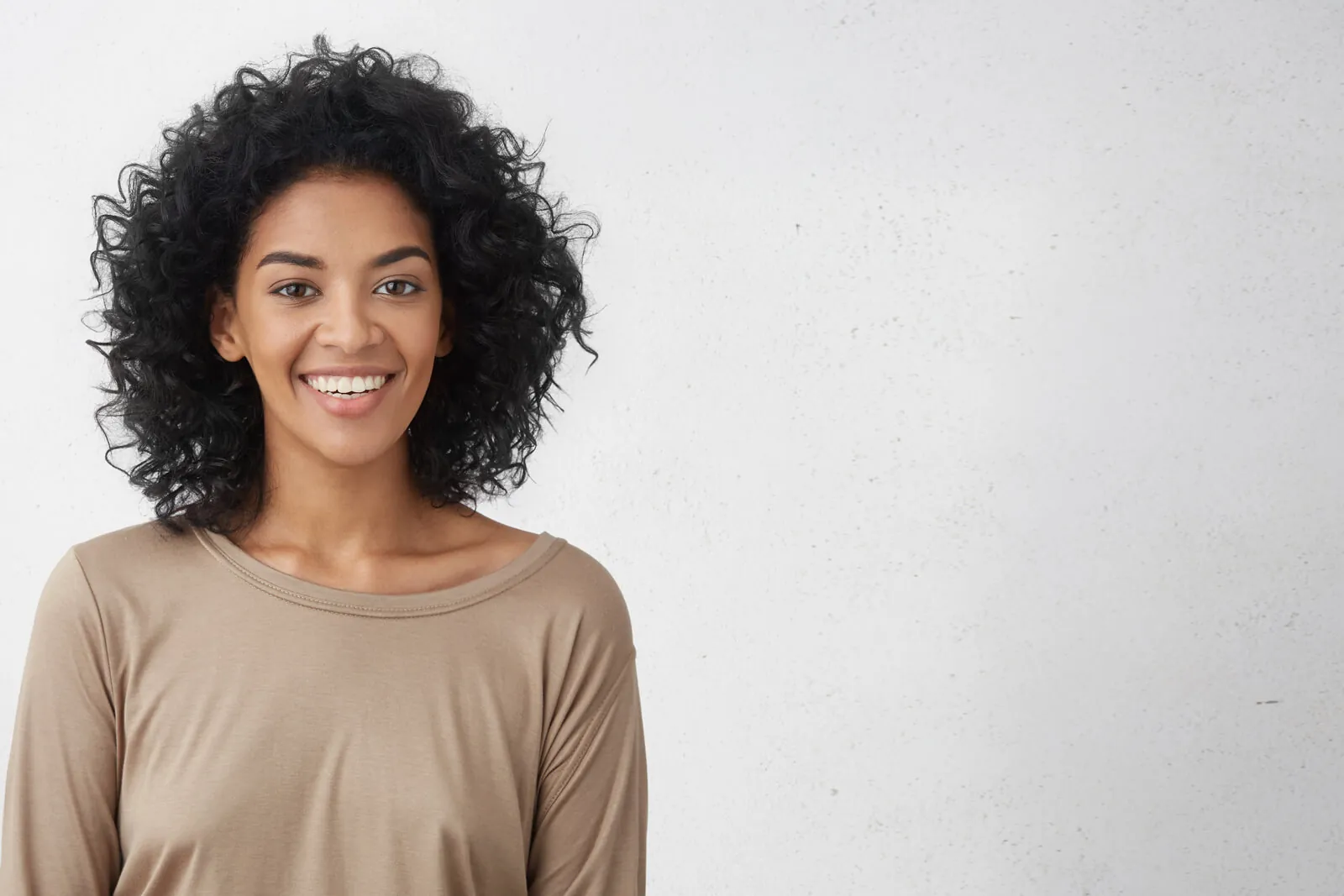 Smiling woman with curly hair in a beige top