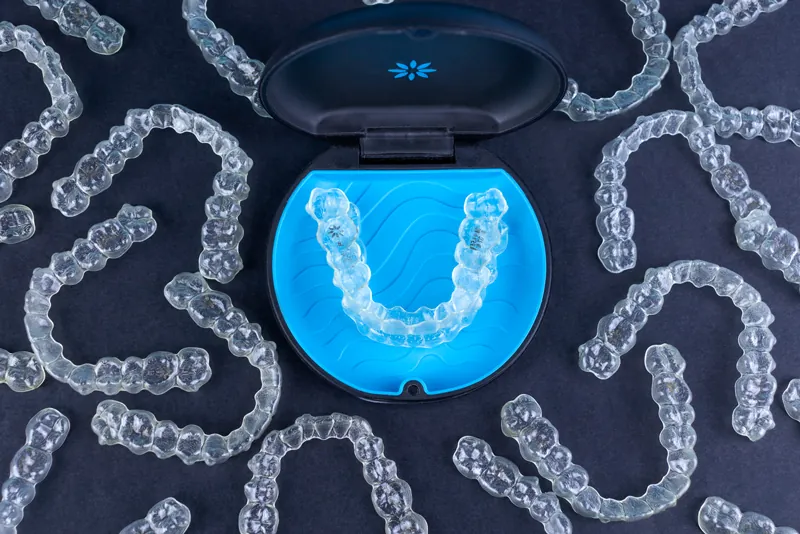 Clear aligners and a blue aligner case laid out on a dark surface
