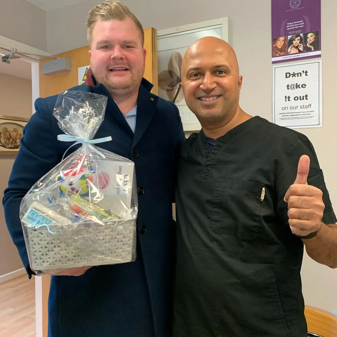 Dr Dave Basrai giving a thumbs up beside a smiling visitor holding a gift hamper