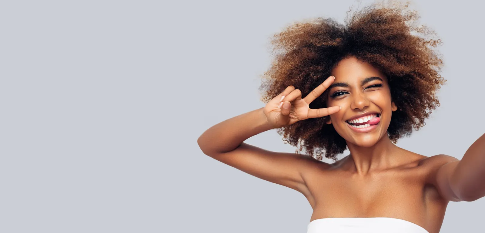 Joyful woman with curly hair making a peace sign, porcelain veneers in Essex