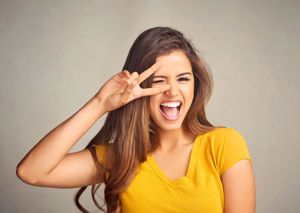 Woman in a yellow T-shirt laughing and making a peace sign