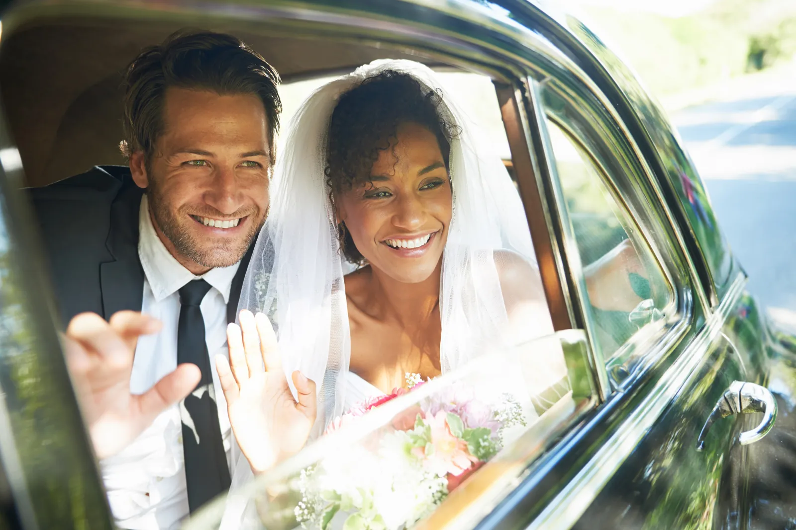 Bride and groom smiling and waving from their wedding car