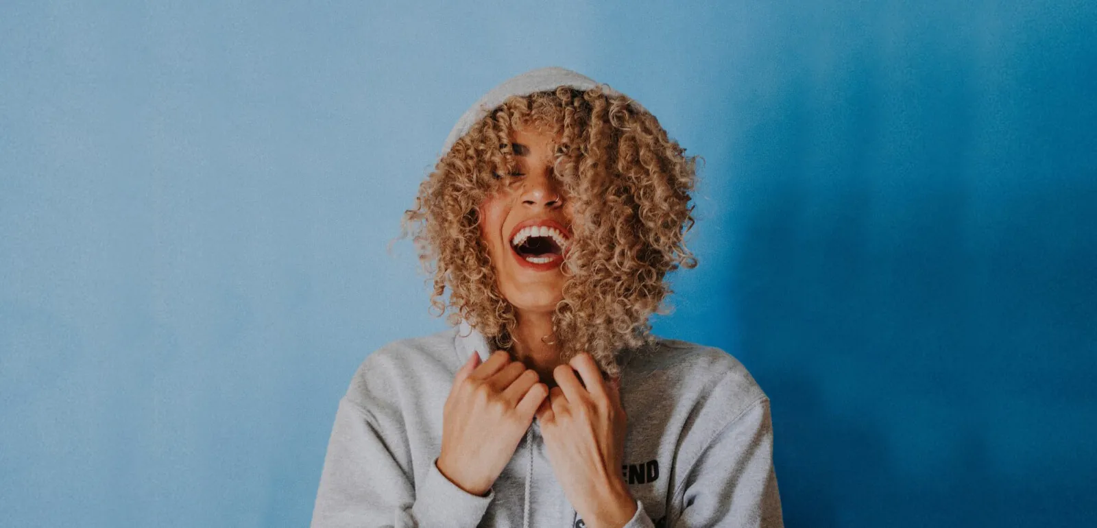 Person with curly hair laughing against a blue background