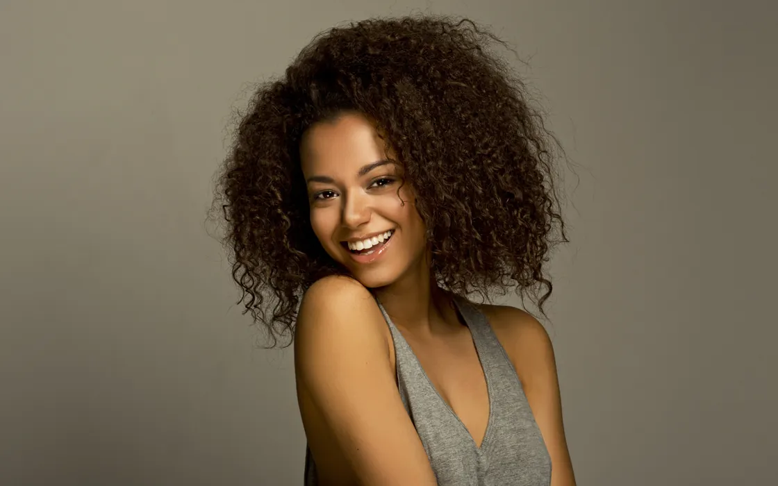 Woman with curly hair smiling in a grey top