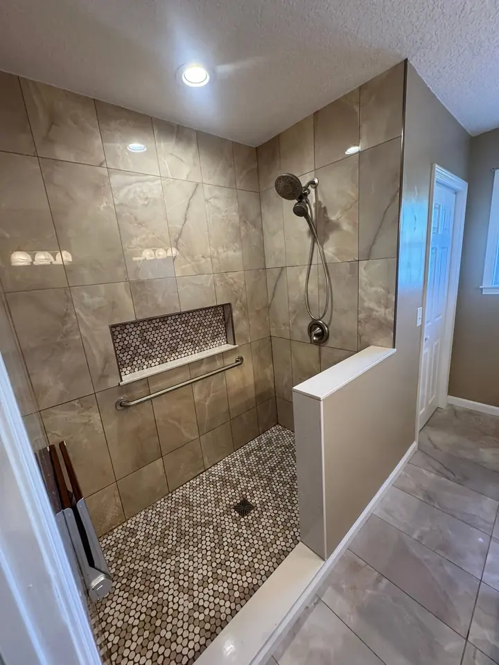 Curbless walk-in shower with marble-look tile, a penny-round tile floor, a tiled niche, a grab bar and a handheld shower